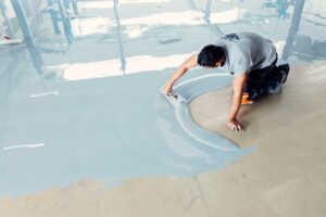 Construction worker on his knees spreading epoxy resin on concrete floor using a trowel